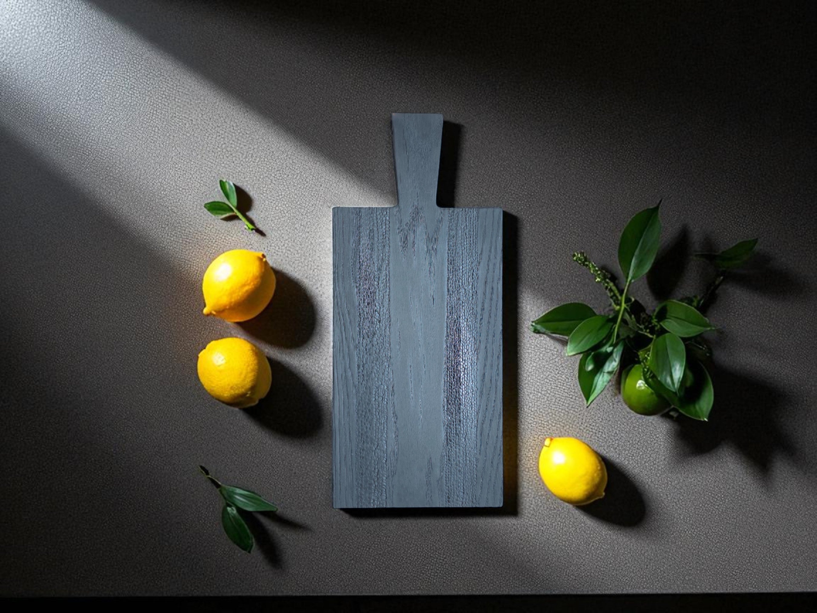 Das handgefertigte Black Snake Board von OLDRYE, perfekt in Szene gesetzt mit frischen Zitronen und Limetten. Ideal zum Servieren von Speisen oder als stilvolles Dekoobjekt in Ihrer Küche.