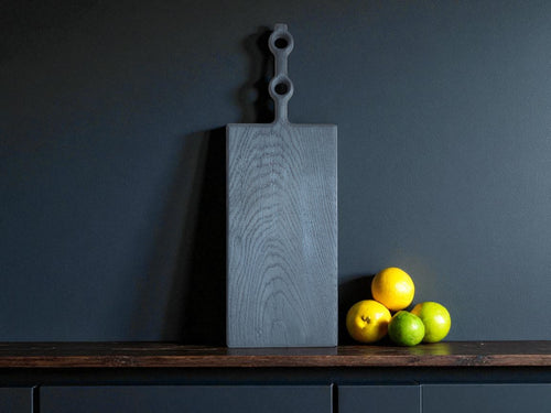  Handgefertigtes, schwarzes Eichenbrett mit Doppelgriff-Design, veredelt im Yakisugi-Verfahren, präsentiert mit frischen Zitronen und Limetten. Ideal als Servierbrett für Käse oder als Deko.
